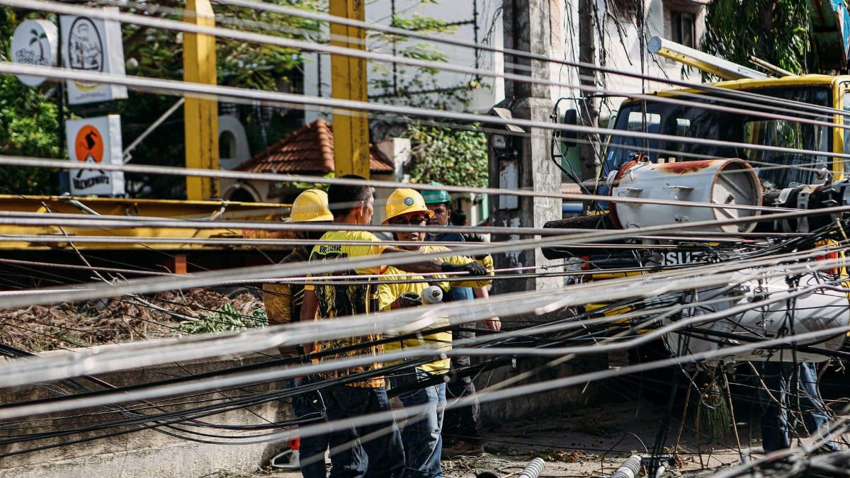 Utility workers repairing downed power lines amidst damaged infrastructure. Outdoor setting with chaos.