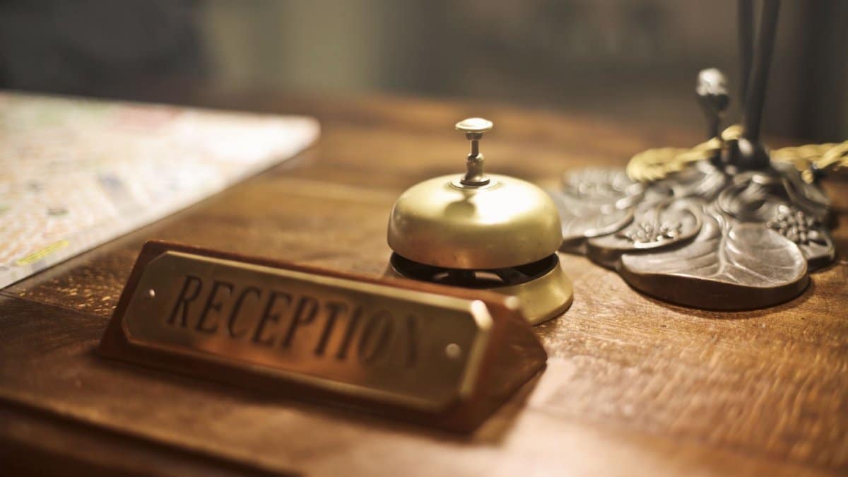 Old fashioned golden service bell and reception sign placed on wooden counter of hotel with retro interior