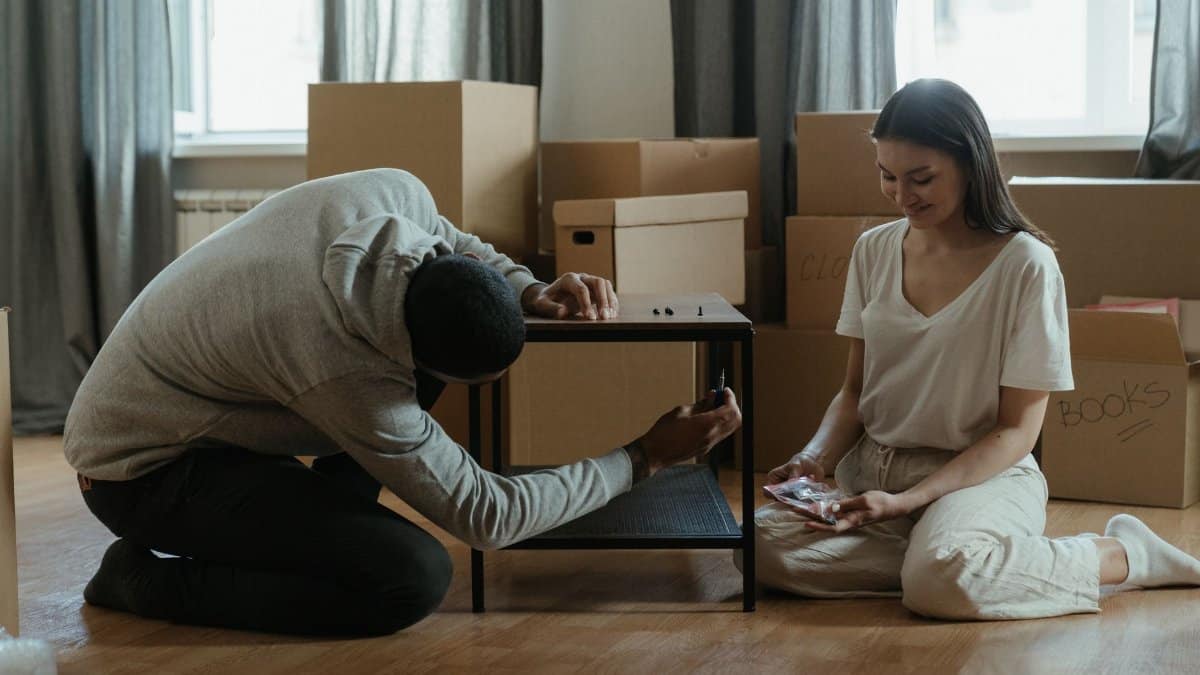 A couple assembling a coffee table amid stacked moving boxes in their new home.
