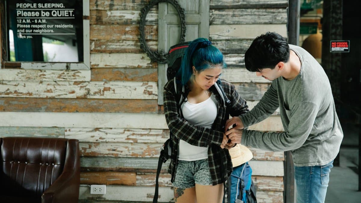 Two travelers prepare their backpacks in a rustic hostel lobby.