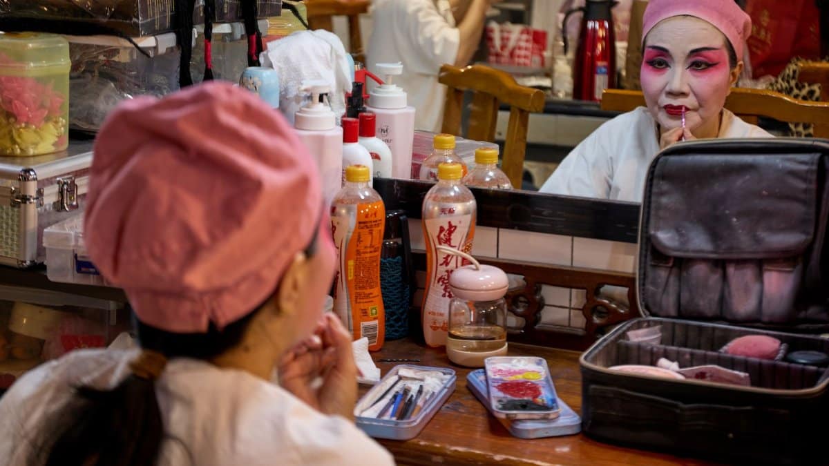 A Chinese opera performer applies makeup backstage in preparation for a performance. Vibrant colors and traditional attire.