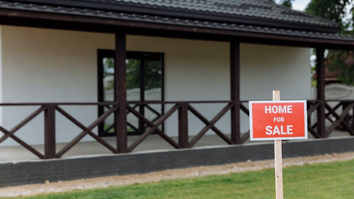 White house with porch and 'Home for Sale' sign on a sunny day.