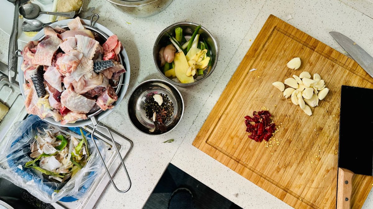 Overhead shot of a kitchen counter with chopped garlic, chicken, and various ingredients for cooking preparation.