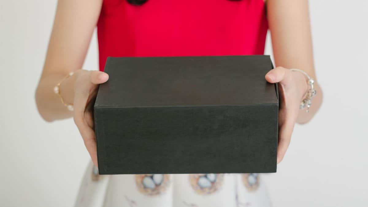 Woman holding a black gift box in a red top, showcasing elegance and surprise.