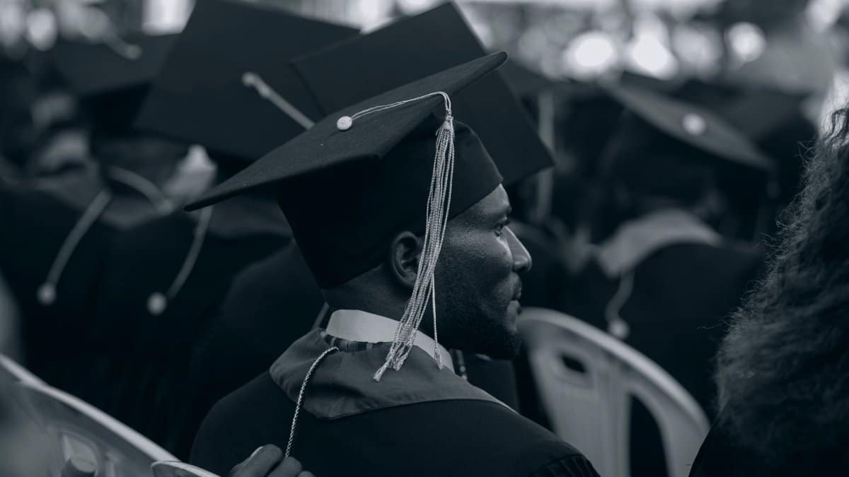 Black and white photo of graduates in caps and gowns at a ceremony.