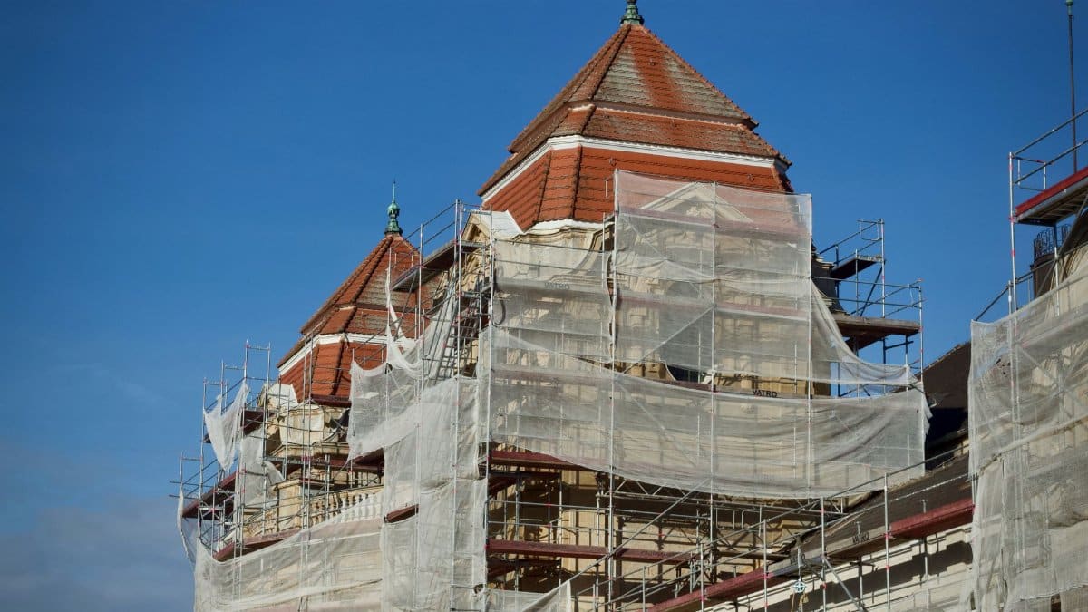 A historic building under restoration, covered in scaffolding and protective nets.