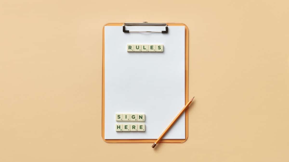 Flat lay of clipboard with letter tiles spelling 'rules' and 'sign here', accompanied by pencil on beige background.