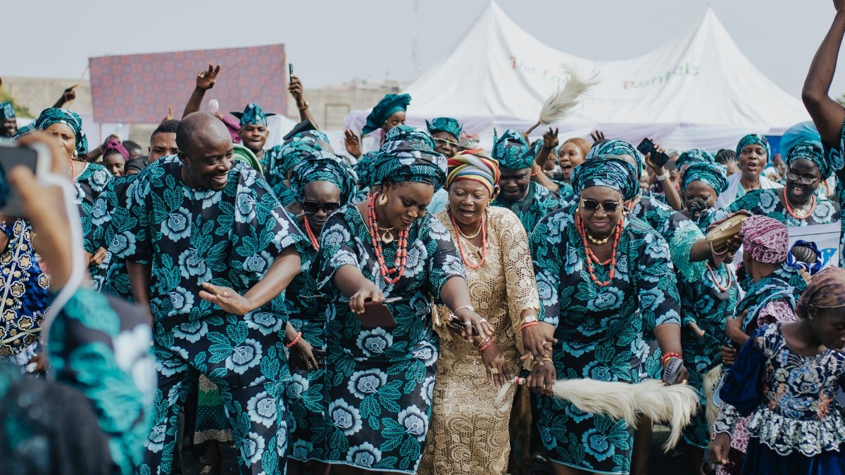 Group of people in traditional African attire dancing joyfully outdoors.