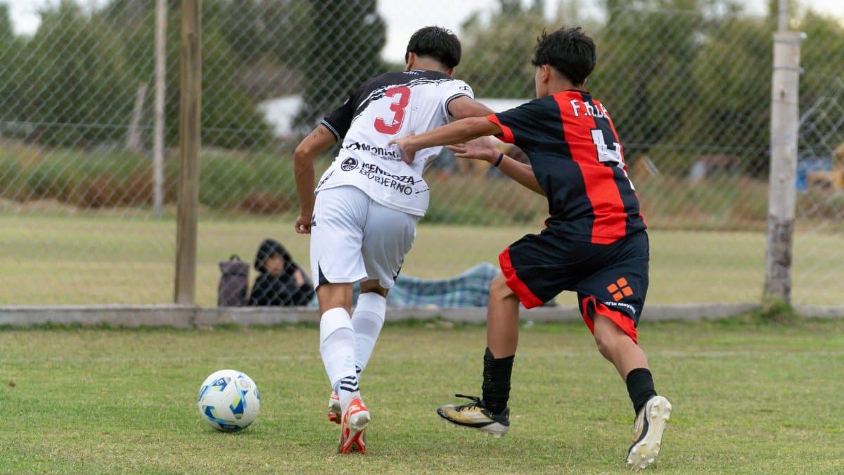 Two teenage boys competing in a soccer match on an outdoor field.