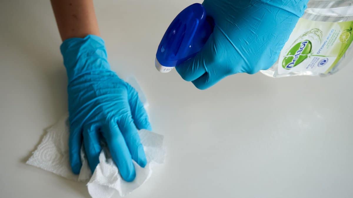 Close-up of hands wearing gloves cleaning a surface with disinfectant spray.