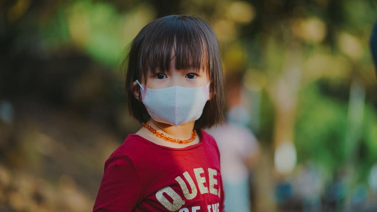 Adorable young girl wearing a face mask outdoors, emphasizing protection during pandemic.