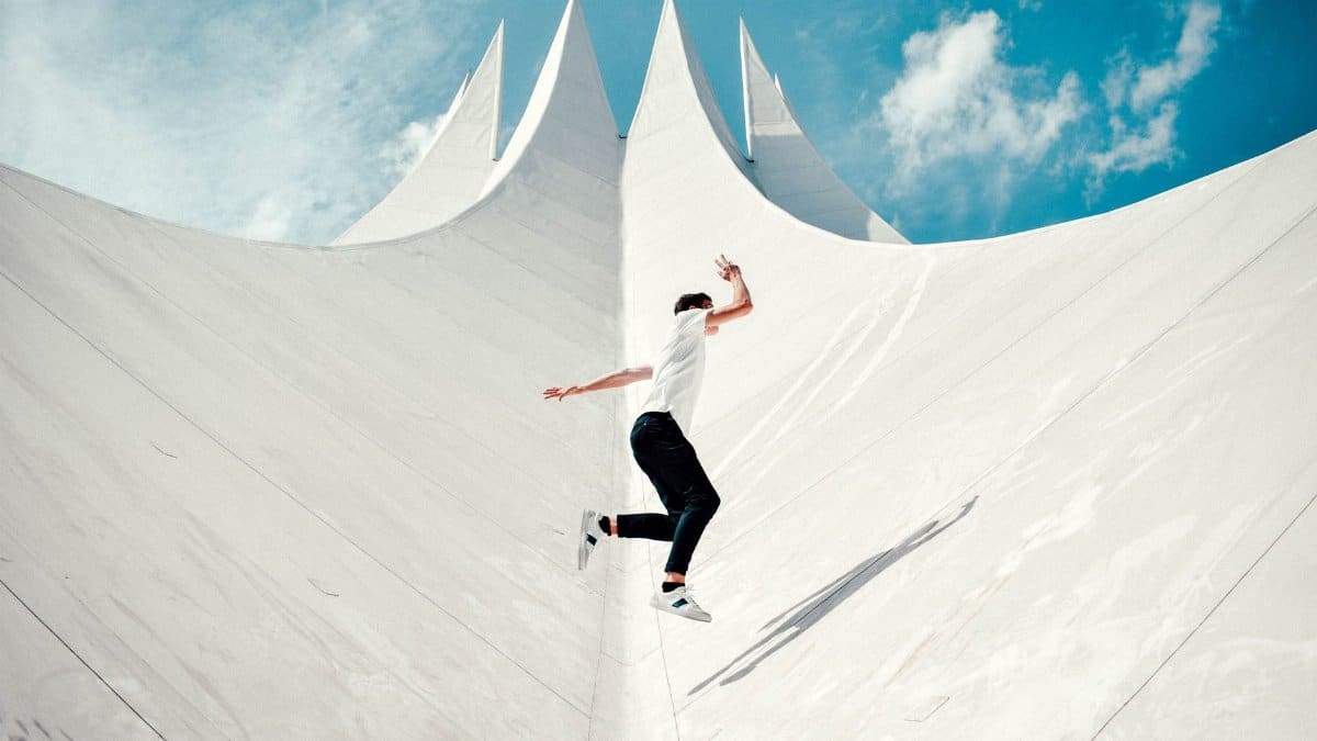 A person in mid-air against a striking modern architectural background under a bright sky.