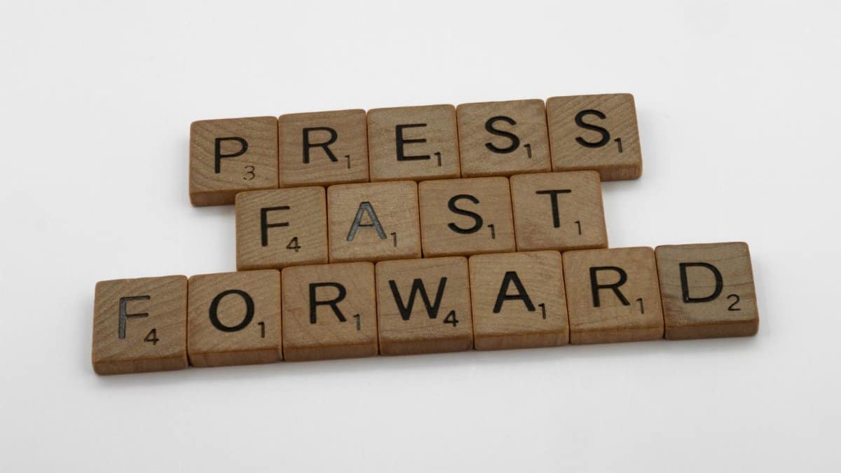 Wooden Scrabble tiles arranged to spell 'Press Fast Forward' on a white background.
