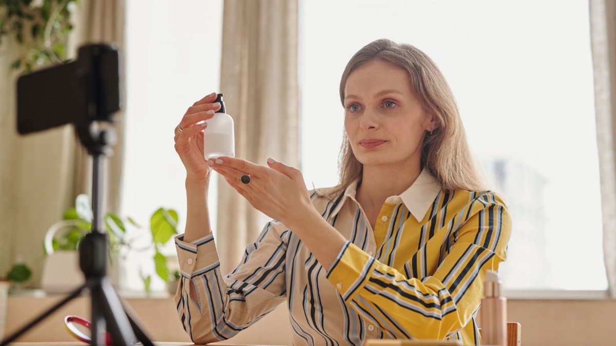 Woman demonstrates skincare product during a vlog in a cozy indoor setting.