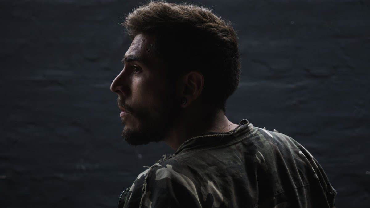 Side profile portrait of a man in low light wearing a camouflage jacket.