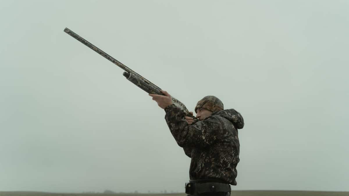 A hunter in camouflage aiming a shotgun in an open field, capturing the essence of outdoor sport.