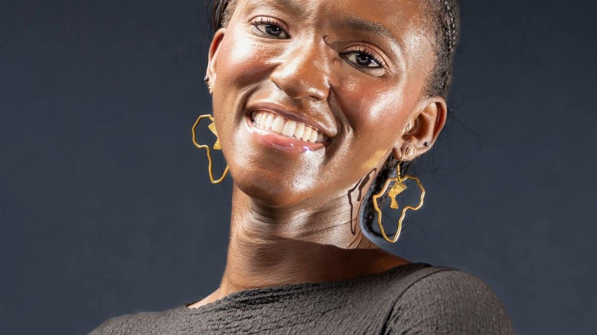 Elegant portrait of a smiling woman wearing unique Africa-shaped earrings against a dark background.