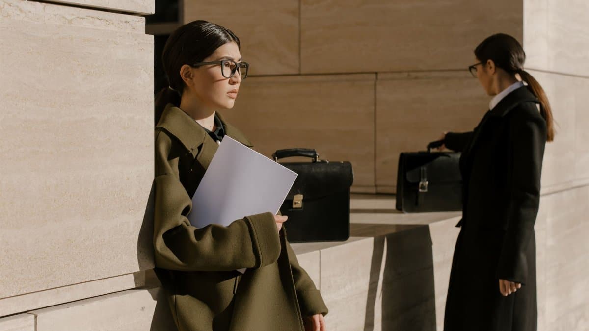 Two women in professional attire with briefcases, outdoors on a sunny day.
