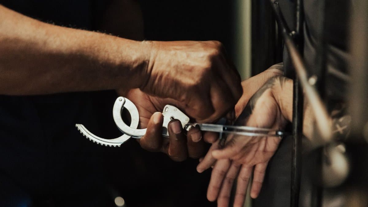 Close-up view of a person being handcuffed in a jail setting, focusing on hands and handcuffs.
