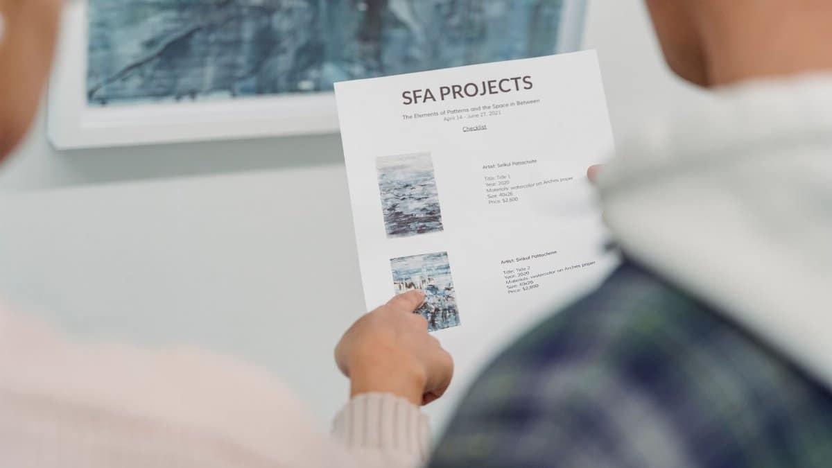 Close-up of hands holding and pointing at a project document during a meeting, featuring artistic project details.