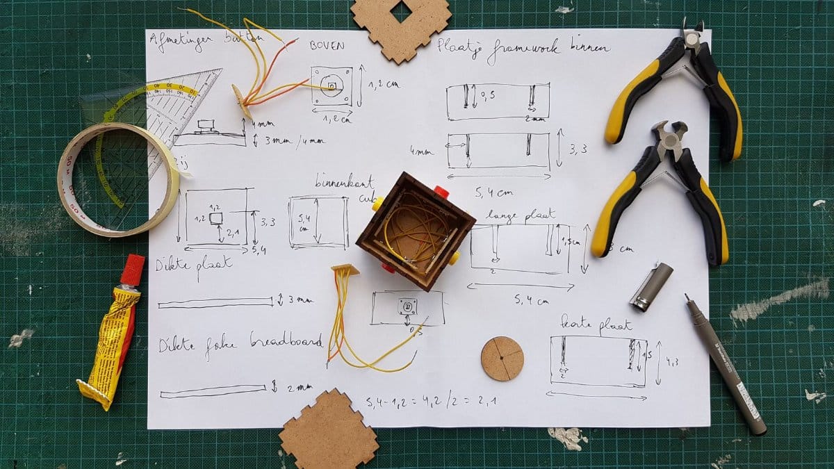 Overhead view of DIY electronics project with components and tools on grid mat.
