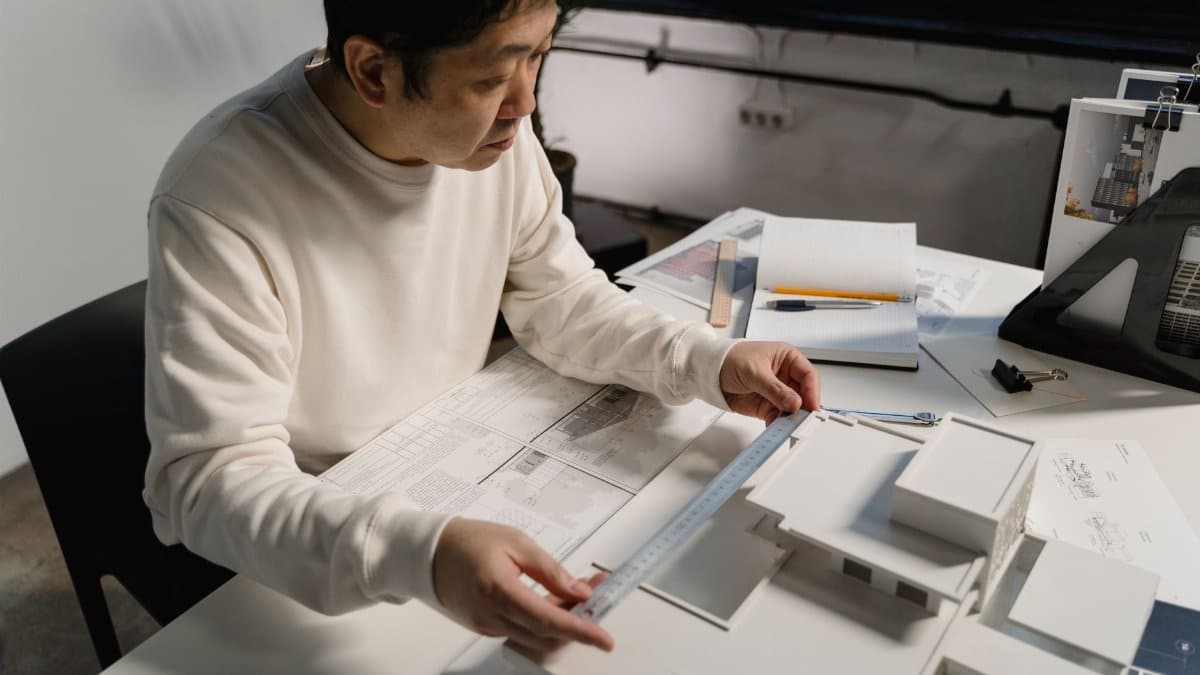 Architect examining a scale model with precision tools at an office desk.