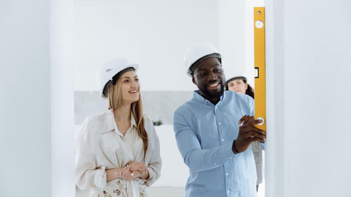 Couple in hard hats using a bubble level during new home construction. Bright indoor setting.