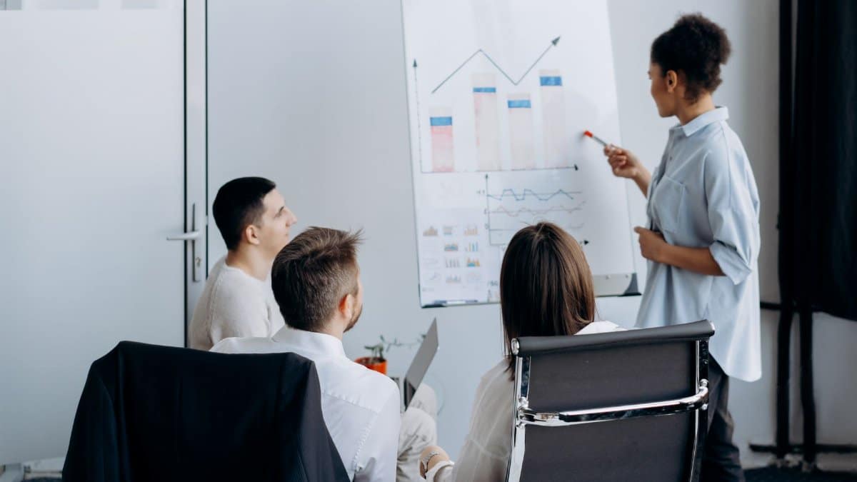 Business team in meeting with presenter discussing charts on a flip board.