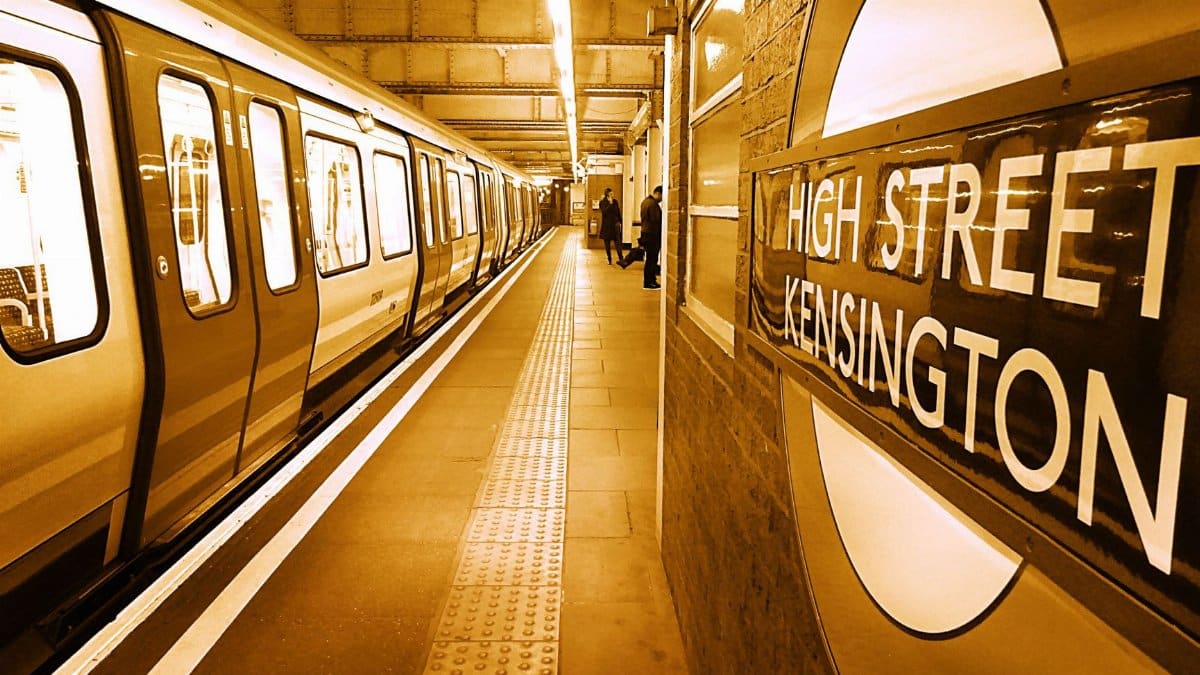A sepia-toned view of High Street Kensington station platform with a train and commuters in London.