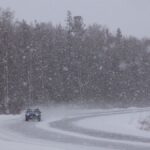 A car navigates a snowy forest road during a winter snowstorm, capturing the harsh weather conditions.