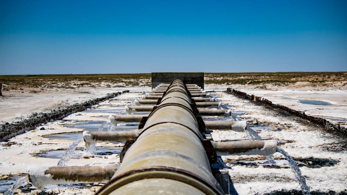 Large industrial pipeline discharging wastewater in arid, rural landscape under clear blue sky.