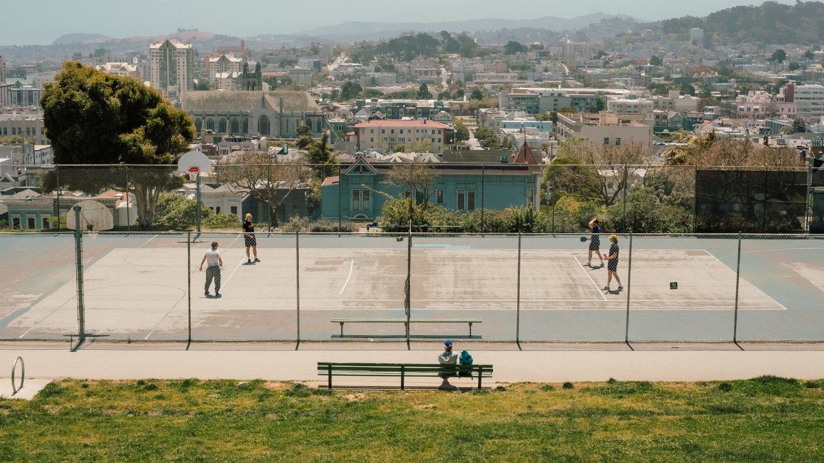 An aerial view of people playing basketball in a park with a cityscape backdrop, showcasing urban recreation.