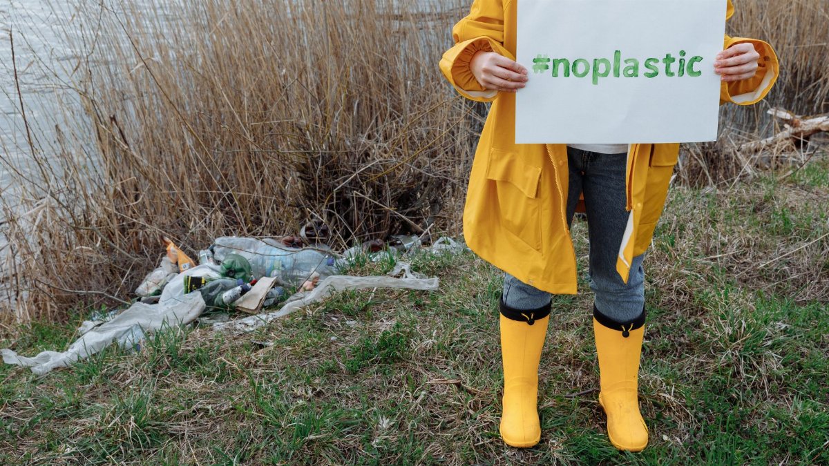 A person in a yellow raincoat holds a #noplastic sign, promoting environmental awareness.