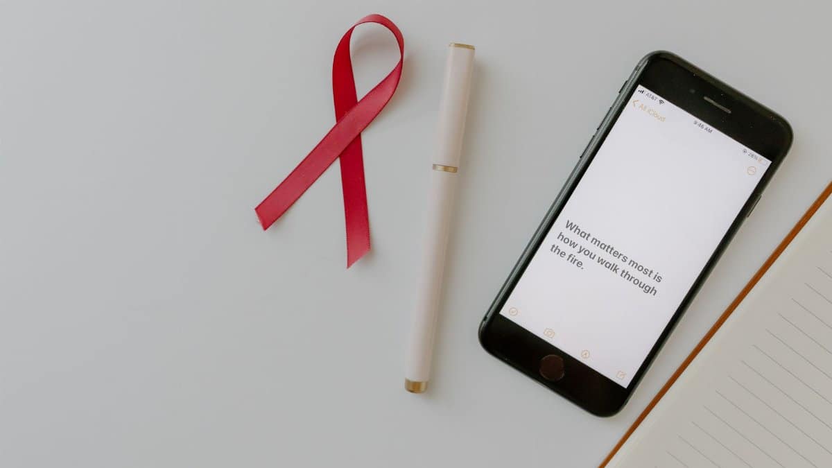 Flat lay of pink ribbon, smartphone, and pen symbolizing breast cancer awareness.