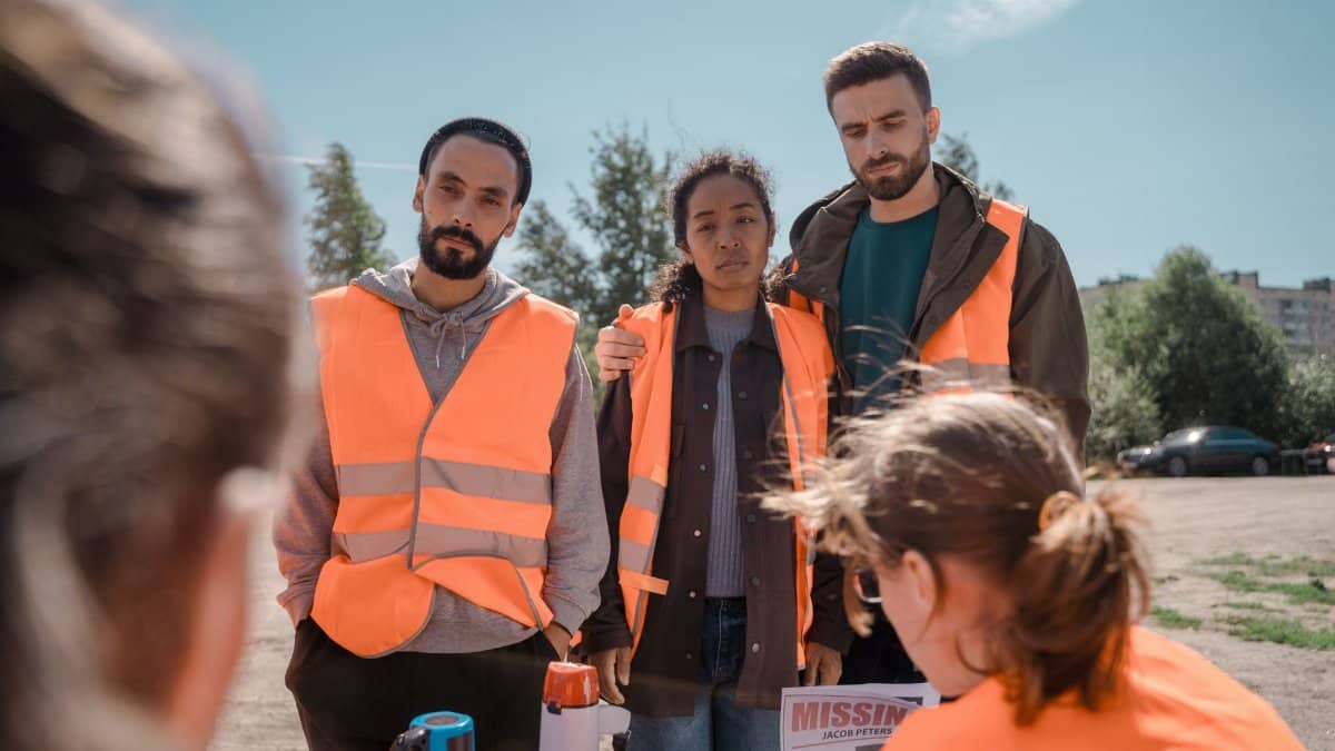 Group of volunteers wearing orange vests coordinating efforts outdoors on a sunny day.