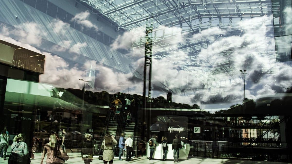 Reflections of clouds and people in a glass urban building, creating a dynamic city scene.