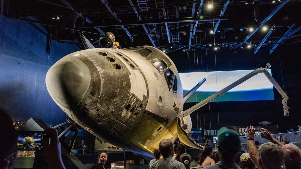Crowd admires Space Shuttle Atlantis at an indoor space museum exhibit.