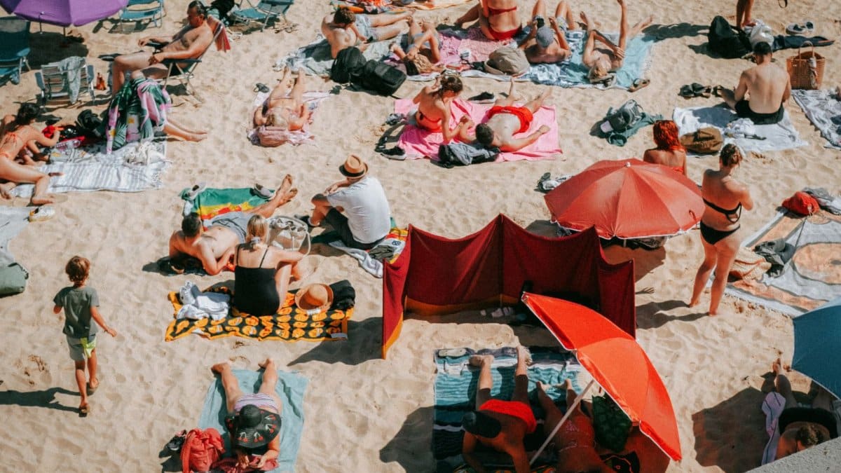 Crowded beach scene on a sunny day in Cascais, Portugal, capturing people sunbathing and enjoying leisure time.
