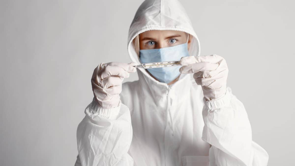 Person in protective suit holding a thermometer during health crisis.