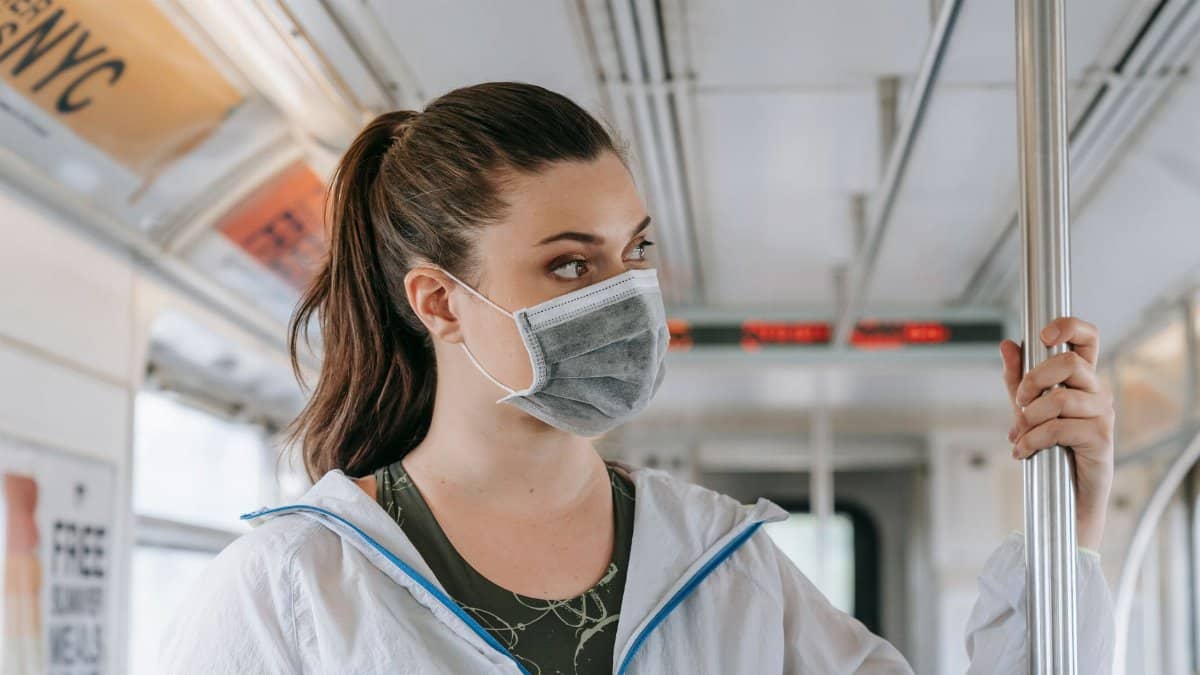 An adult woman wearing a face mask rides public transportation, focusing on safety and protection.