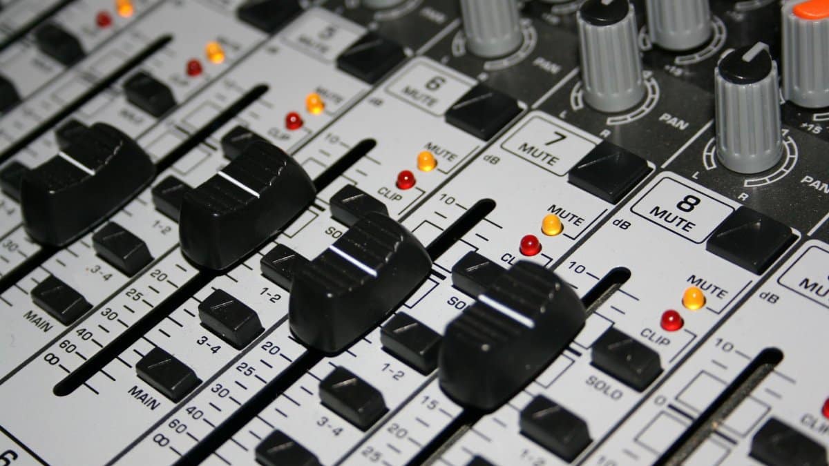 Detailed shot of a professional audio mixer with knobs and sliders illuminated by indicator lights.