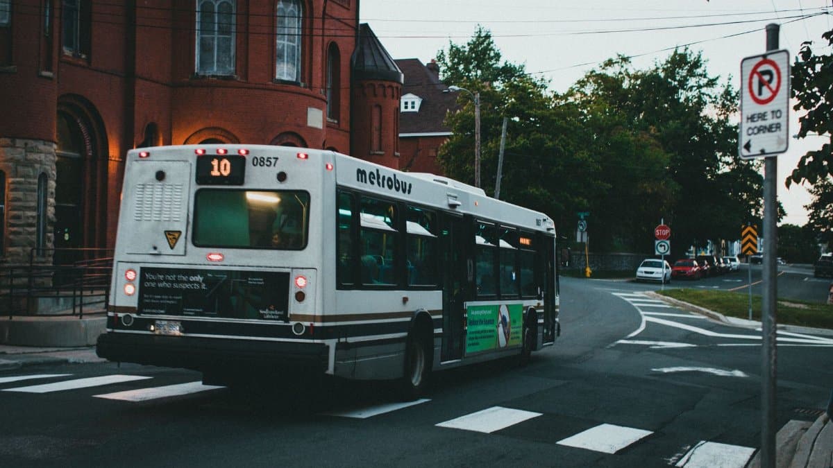 A metrobus rides through urban streets near red brick buildings at dusk, reflecting public transit in a cityscape.