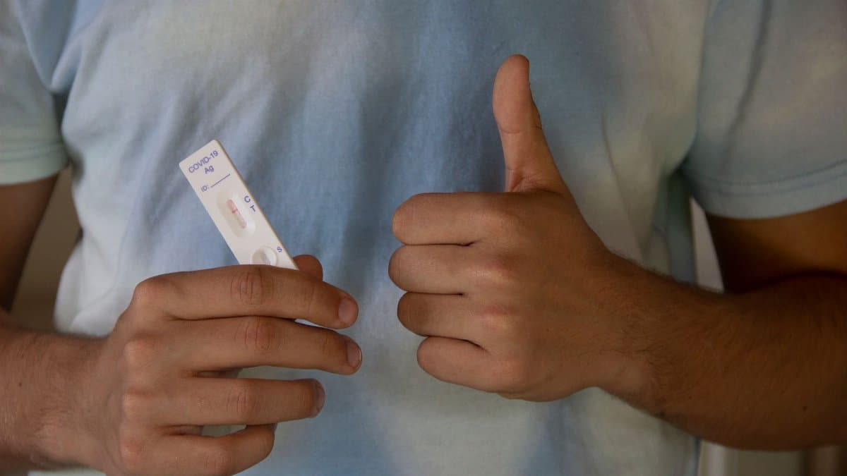 A person showing a COVID-19 antigen test and giving a thumbs up, indicating a negative result.