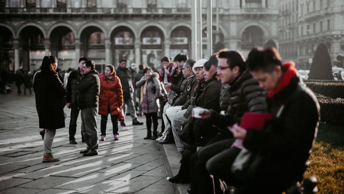 A group of people in winter attire gathering in a street scene in Milan, Italy.