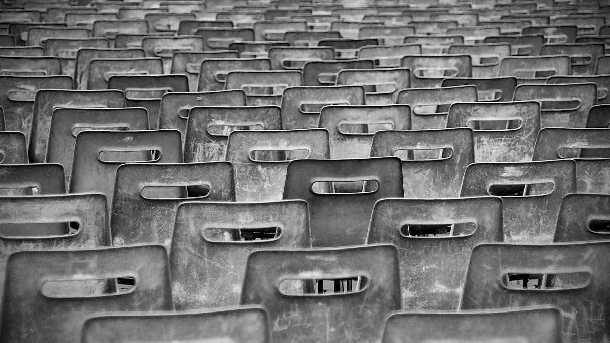 Black-and-white image of empty plastic chairs arranged in rows, creating a pattern.