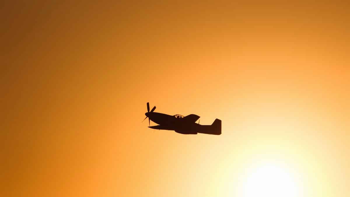 A military airplane silhouette flies across a vibrant sunset in İzmir, Türkiye.