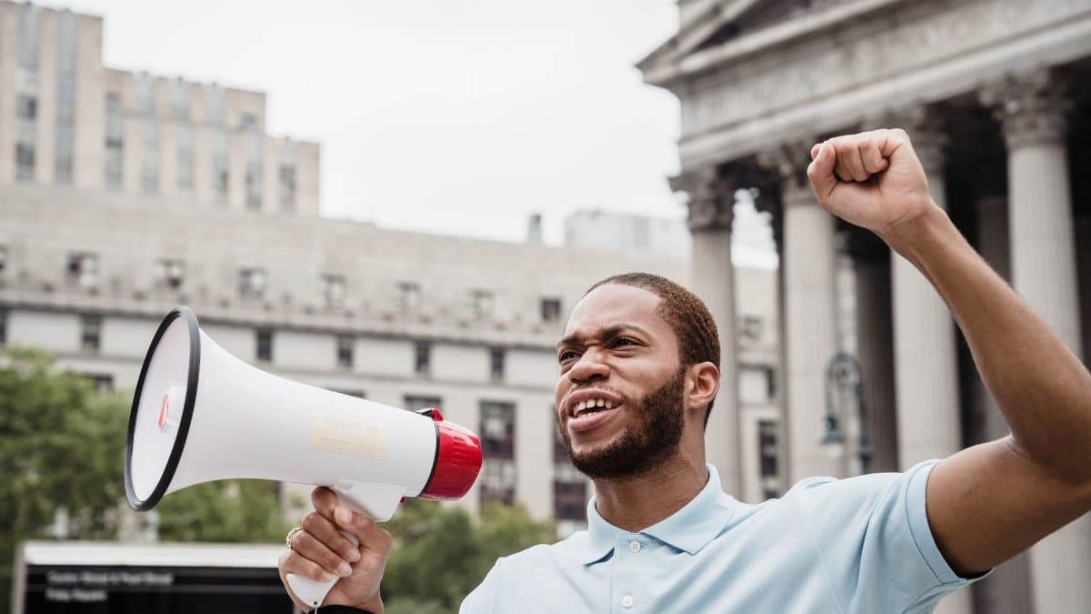 A young African American man passionately protests with a megaphone in an urban setting.
