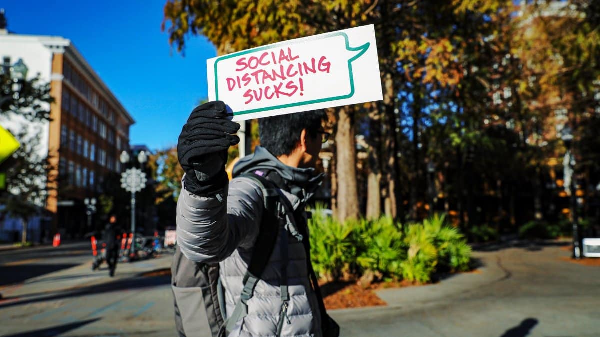 Person outdoors in Orlando holding a sign saying 'Social Distancing Sucks!'.