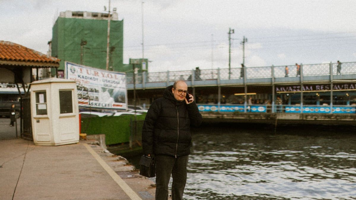 Man in a black jacket using a phone by the Istanbul waterfront near Galata Bridge.