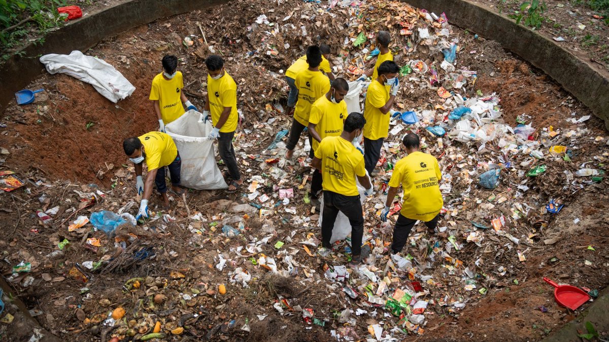 A group of volunteers in yellow shirts clean up a large waste pit outdoors, demonstrating teamwork and environmental care.
